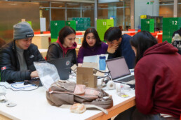 Imagen de estudiantes al rededor de una mesa mirando sus respectivos computadores.